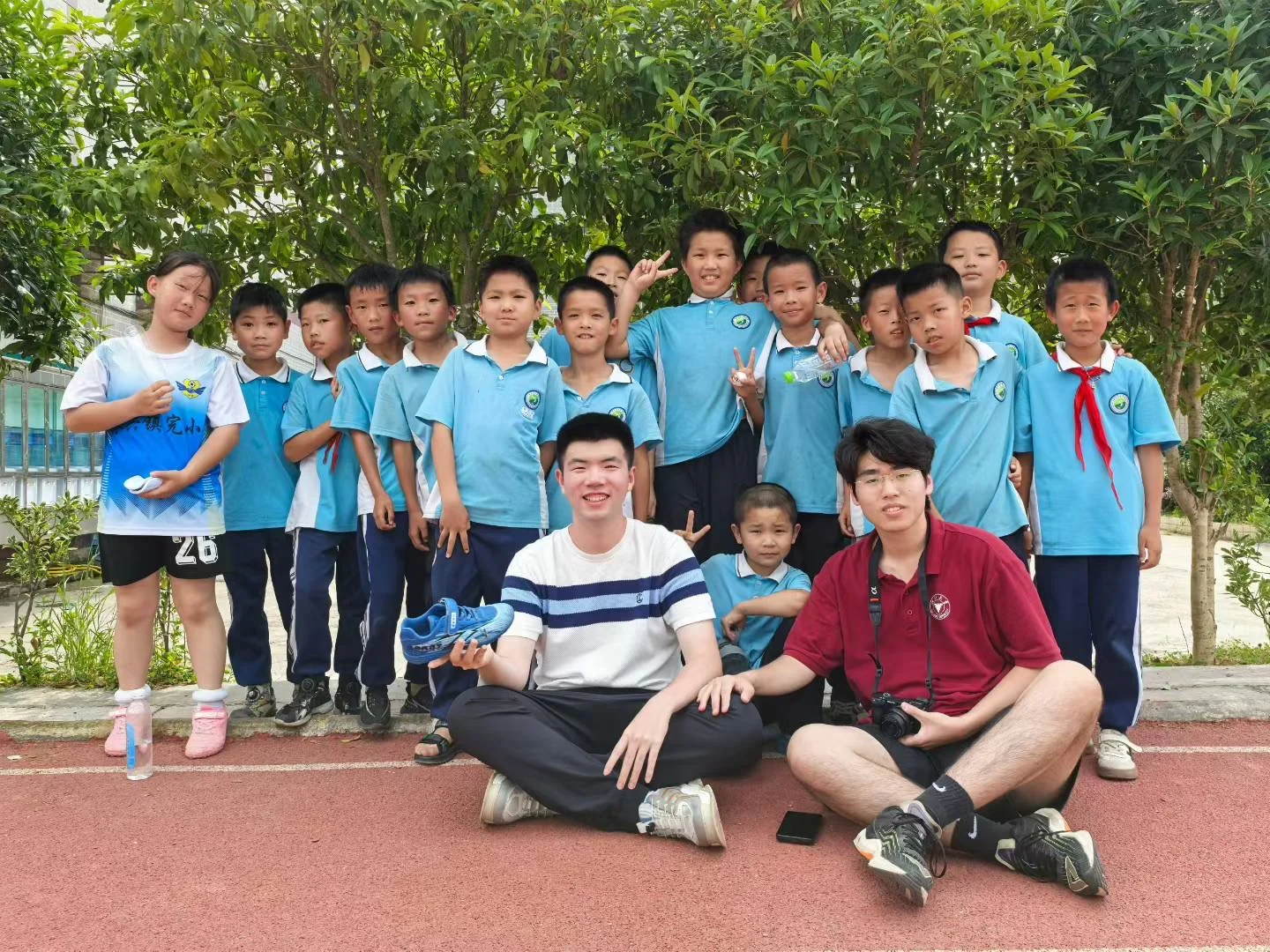 Volunteer teachers and students gathered beneath trees in a schoolyard in Meitan